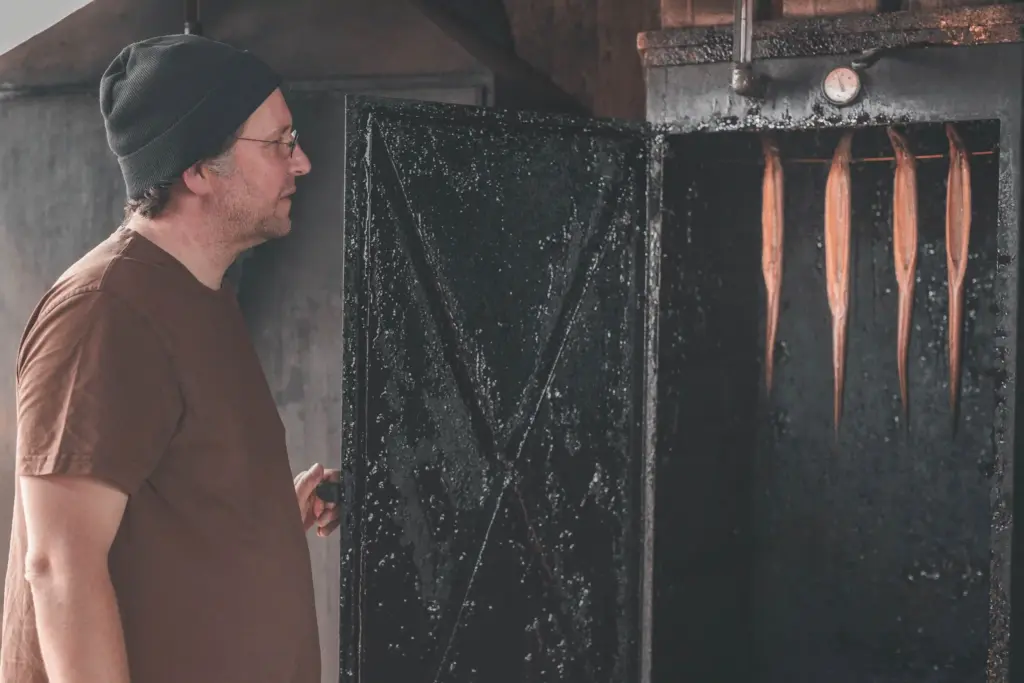 Jörg Sieber, Inhaber der Fischzucht Kroppen, blickt in den geöffneten Räucherofen voller frischem Fisch