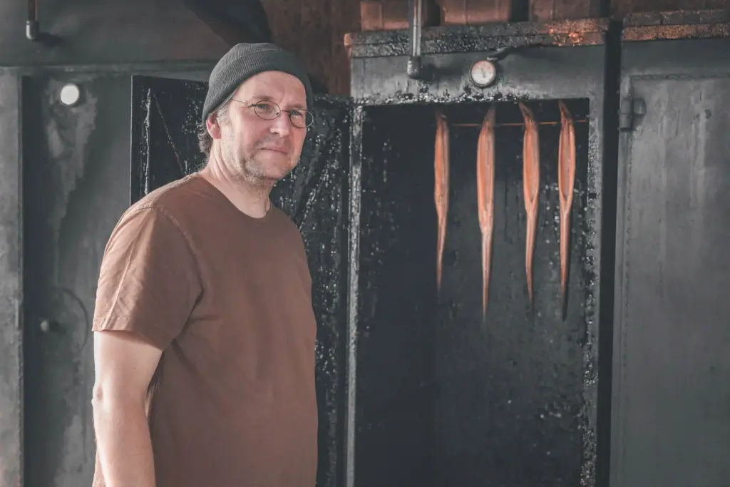 Portrait von Jörg Sieber, Inhaber der Fischzucht Kroppen, neben dem Räucherofen