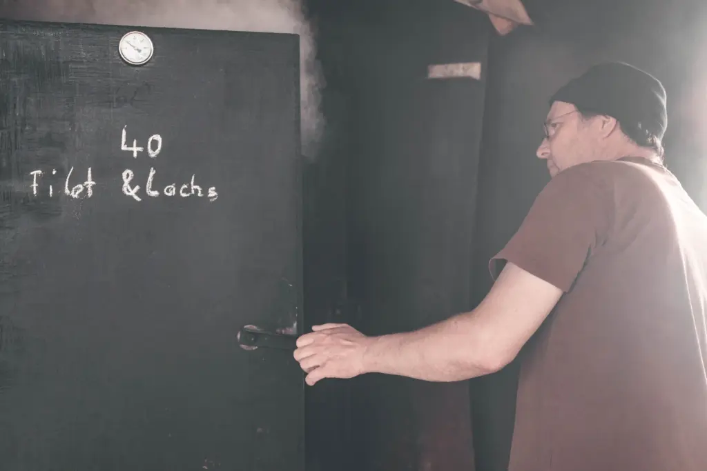 Jörg Sieber, Inhaber der Fischzucht Kroppen, öffnet den traditionellen Räucherofen der Fischzucht Kroppen mit der Aufschrift "Filet & Lachs"